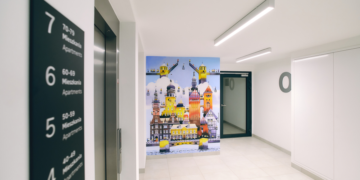 Wnętrze budynku, kolorowy mural na ścianie przestawiający historyczne budynki Elbląga